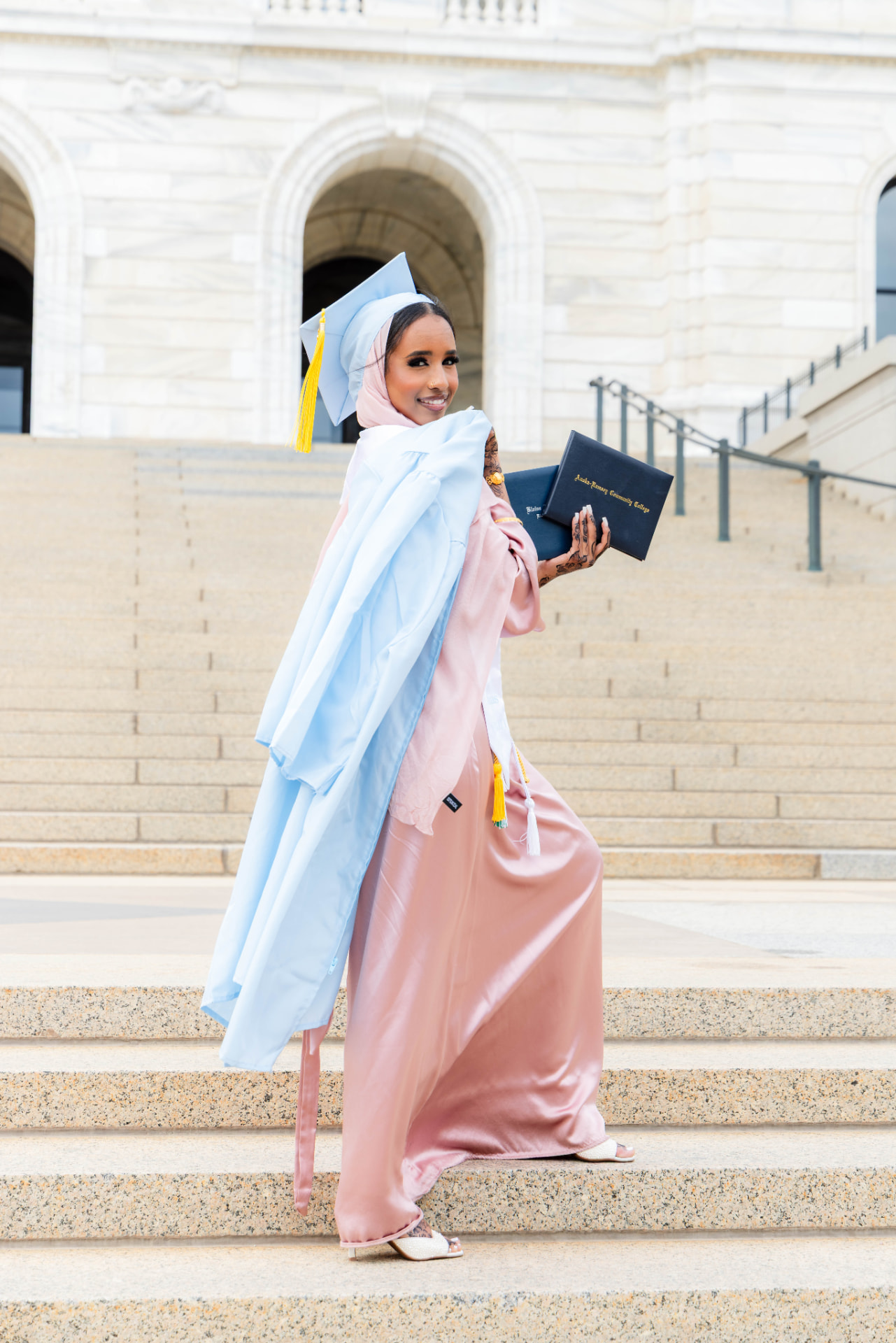 Graduate in blush satin holding her diploma on the Minnesota State Capitol steps