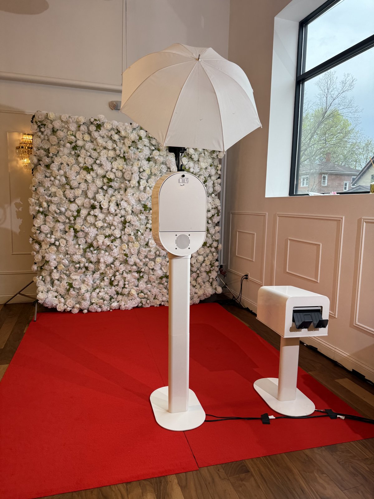 Photo booth with umbrella light, instant print station, white flower wall and red carpet